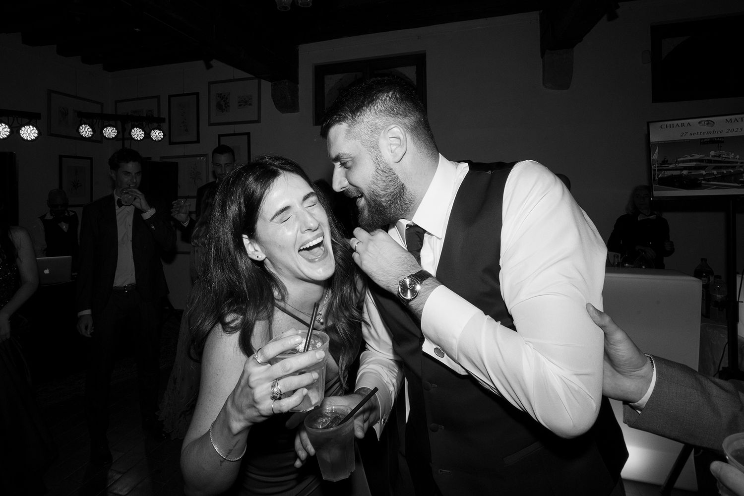 Wedding party guests dancing and celebrating in a dimly lit reception venue.