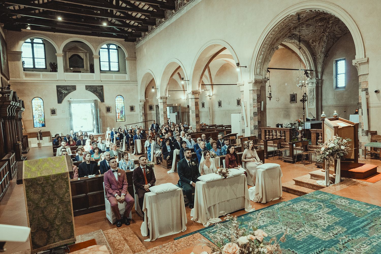 Wedding guests gather in a historic church with arched ceilings and ornate architecture for a ceremony.