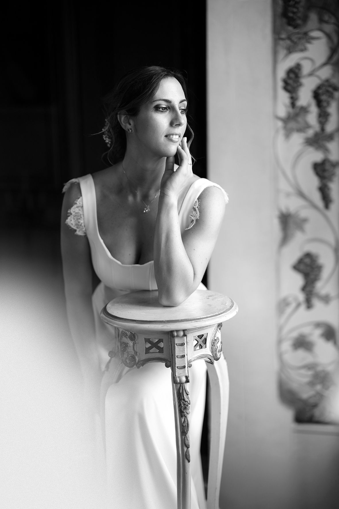 Artistic black and white portrait showing a white dress against an ornate backdrop with soft lighting.