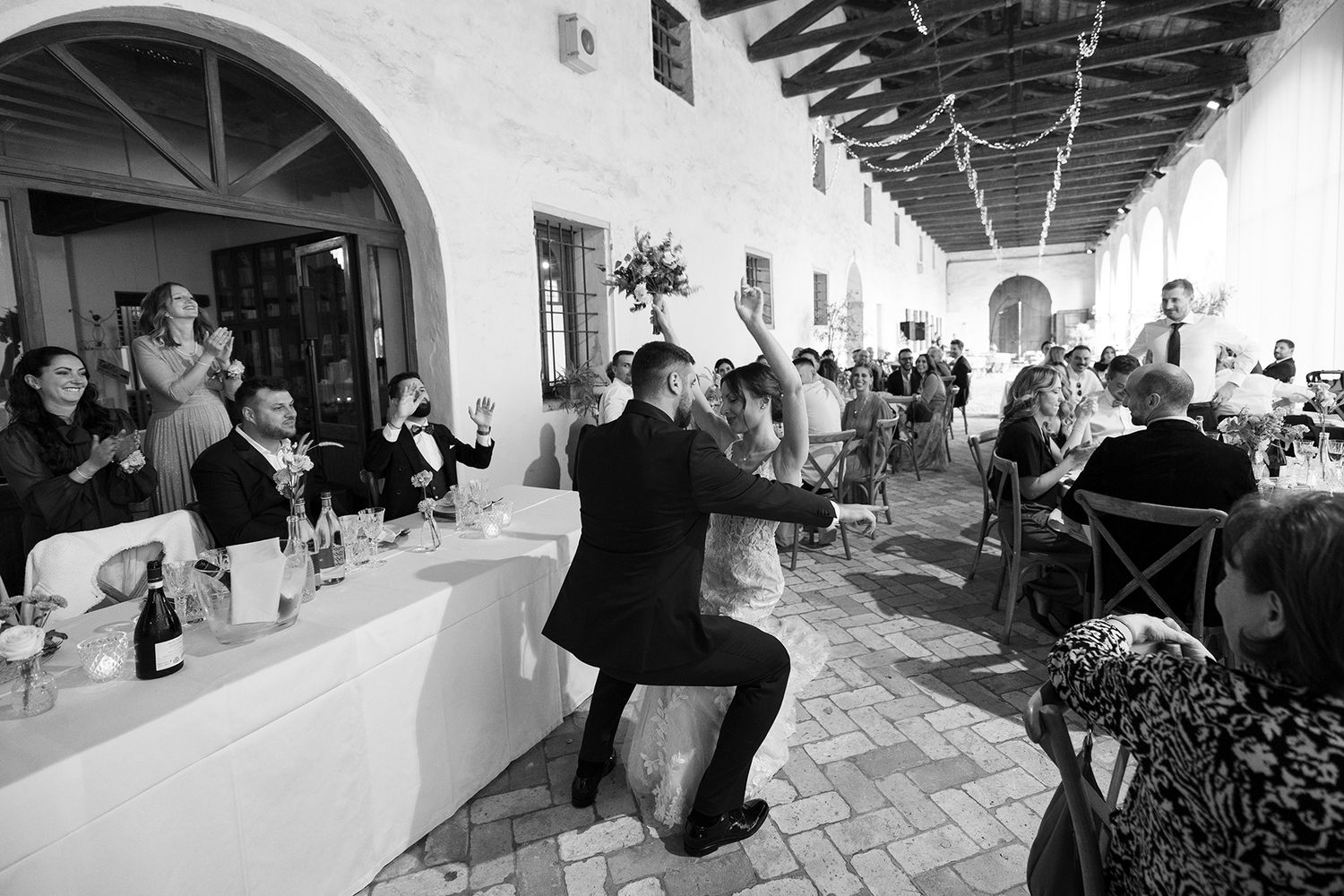 Wedding photographer kneeling to capture shots during reception in black and white.