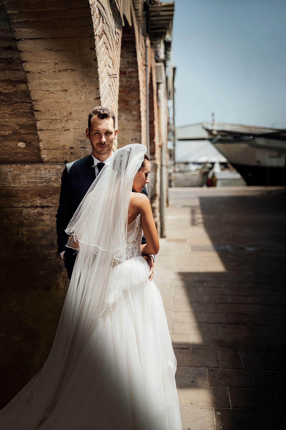A romantic wedding photo captured against rustic architecture with flowing white veil and dress.