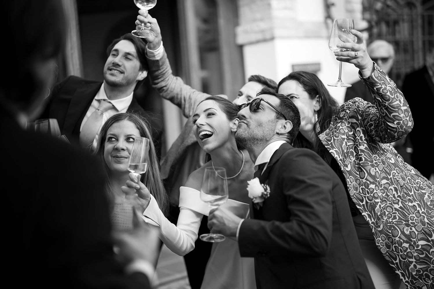 Wedding party raises glasses in celebration during an outdoor toast in black and white.