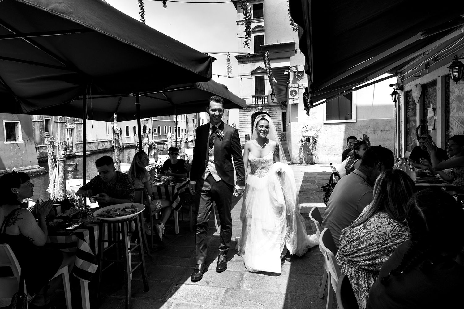 Wedding celebration scene with guests under outdoor tent canopy.