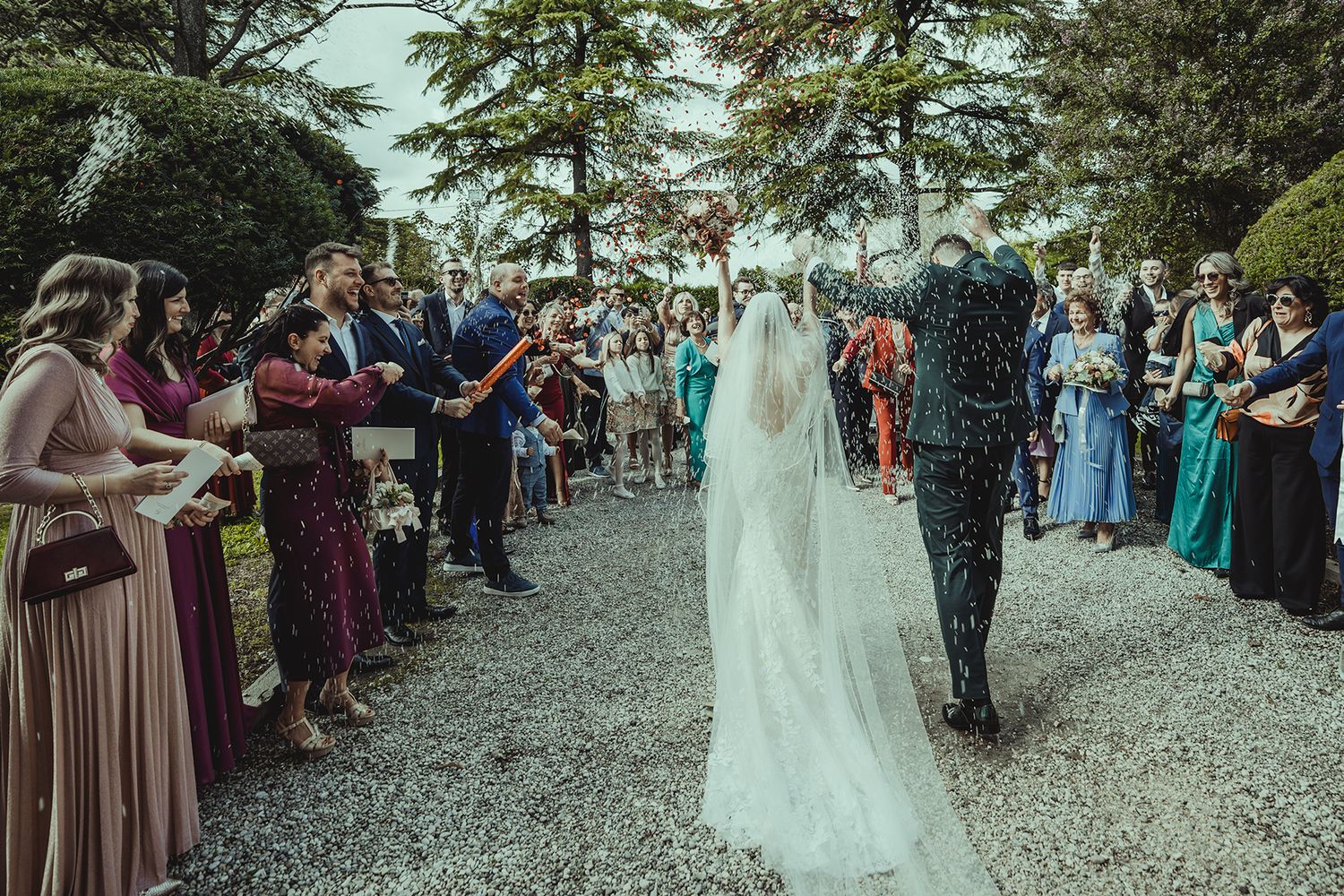 Wedding guests line a gravel path outdoors as they celebrate during a beautiful outdoor ceremony.