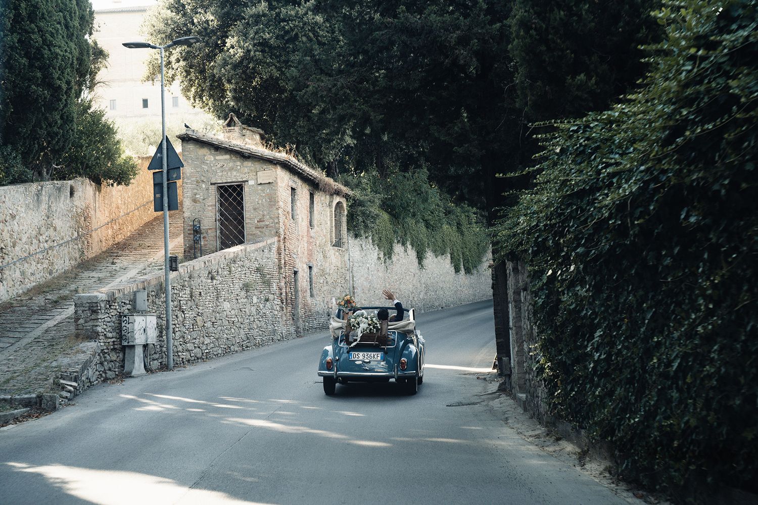 Classic vintage car drives down narrow Italian street lined with stone walls.