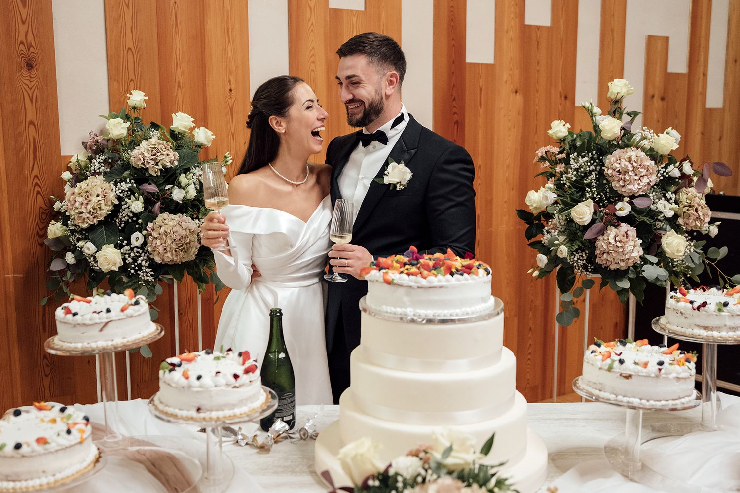 Wedding cake cutting scene with floral decorations and wooden backdrop.