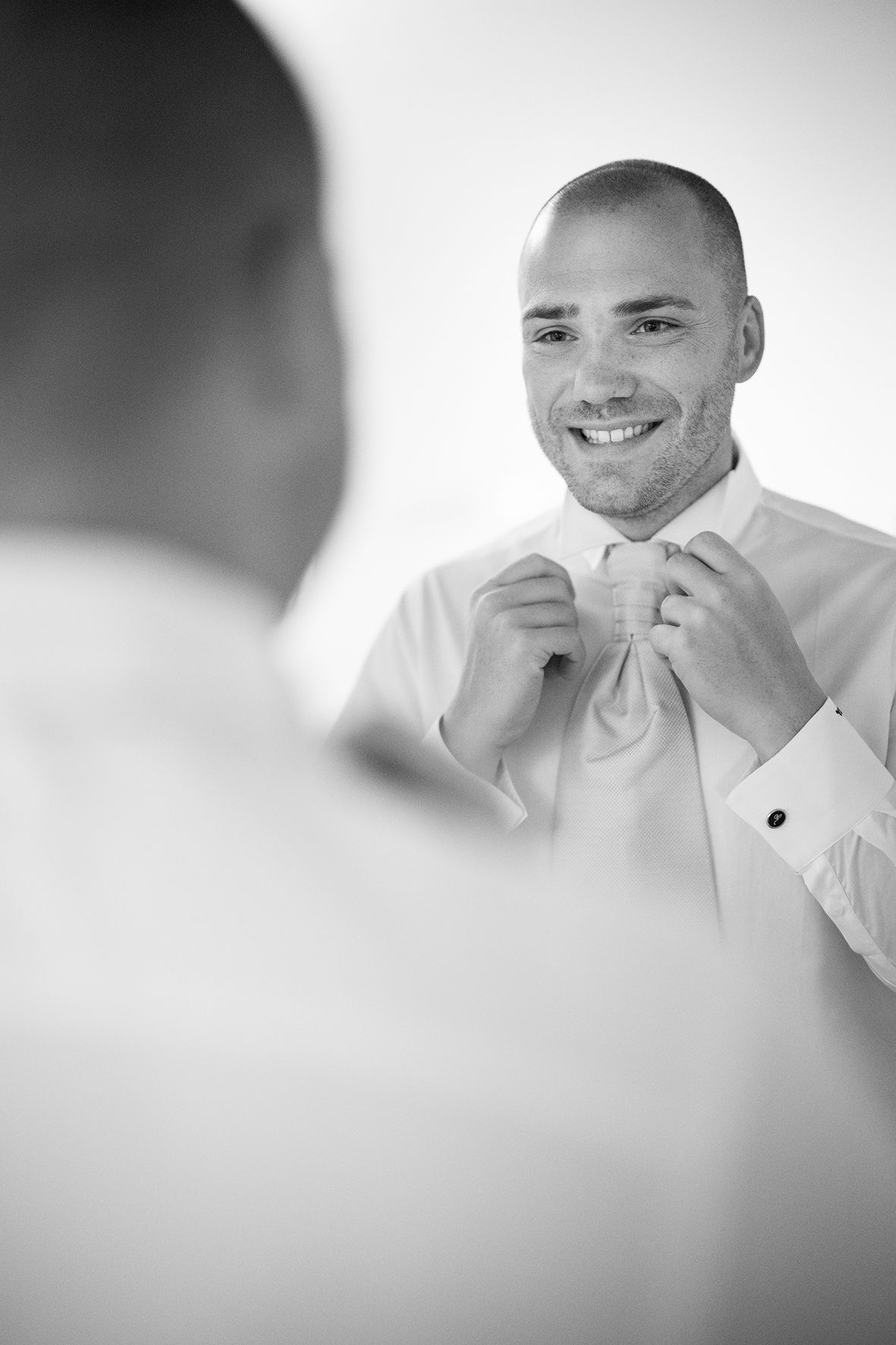 Man in white shirt adjusts his tie while looking in mirror getting ready.