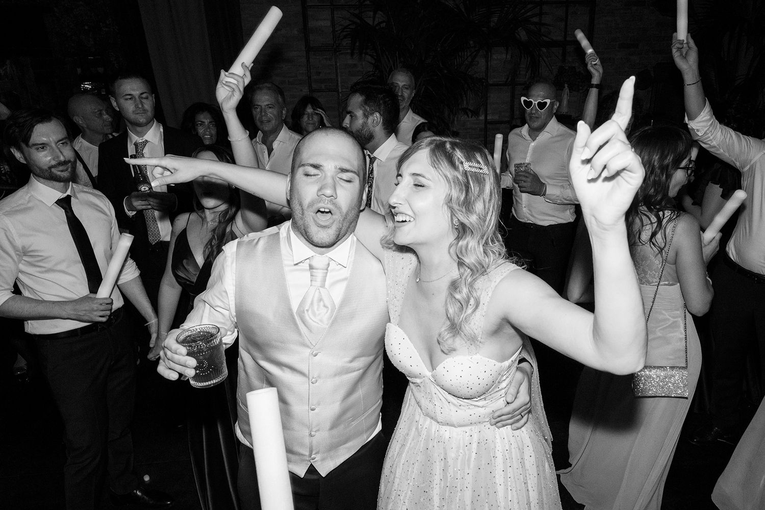 Wedding party dancing enthusiastically with raised arms on the dance floor.