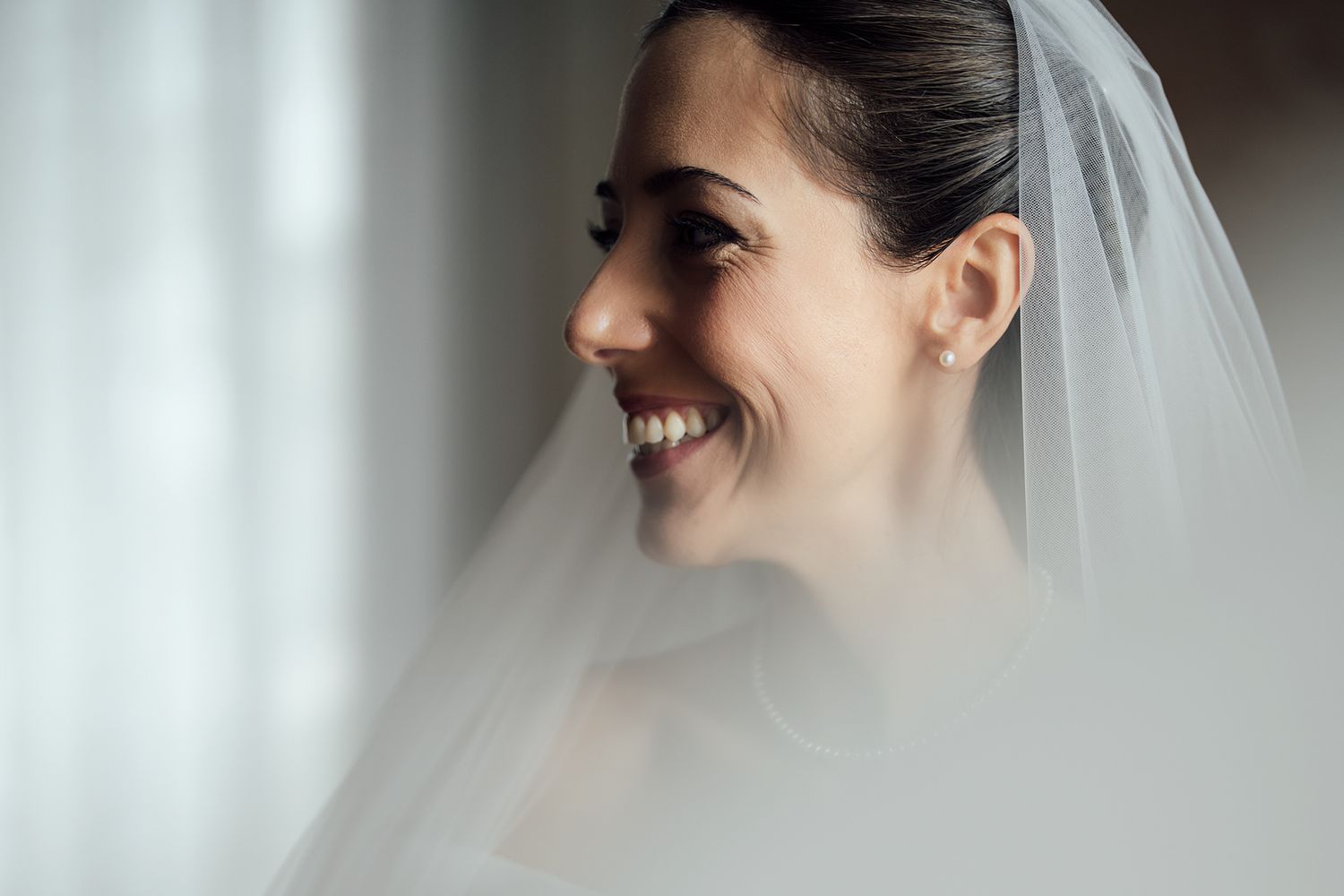 Candid moment through sheer veil showing joyful expression on wedding day.