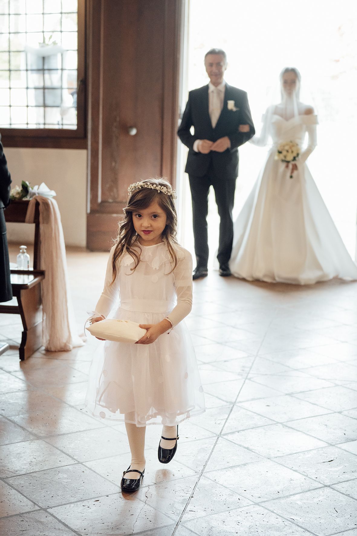 Young flower girl in white dress twirling on tiled floor during wedding ceremony.