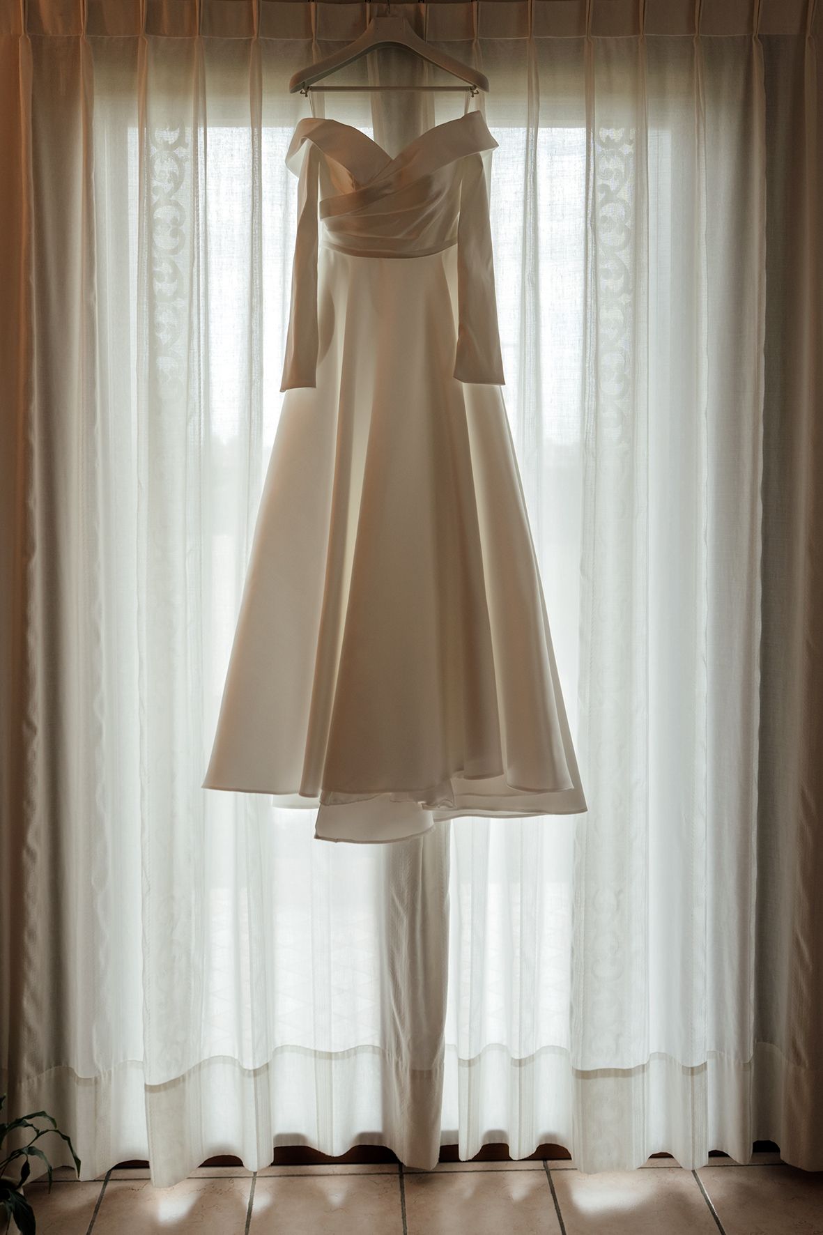 White wedding dresses hanging in row against sheer curtained window with natural light.