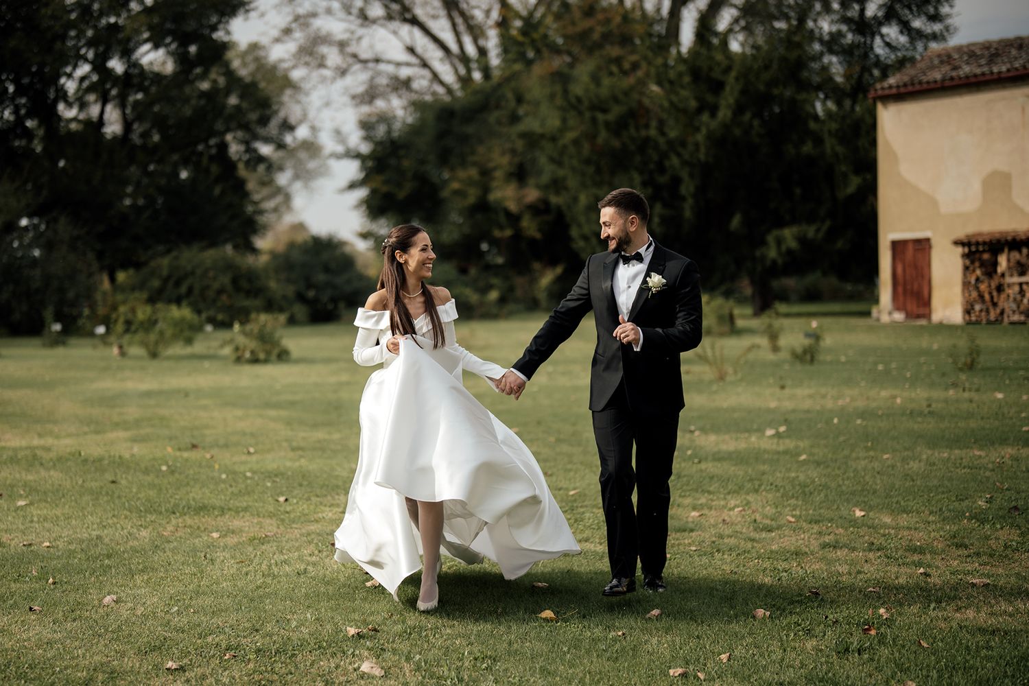 Bride and groom playfully running across a sunny green lawn.