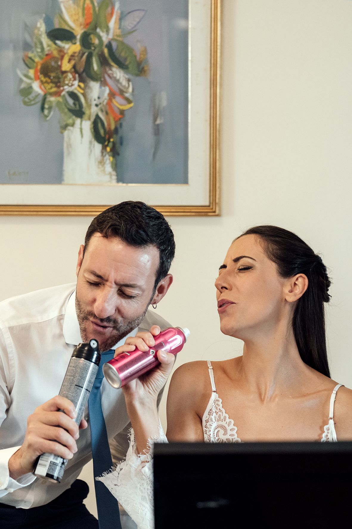 Couple playfully drinking from cans while dressed in wedding attire.