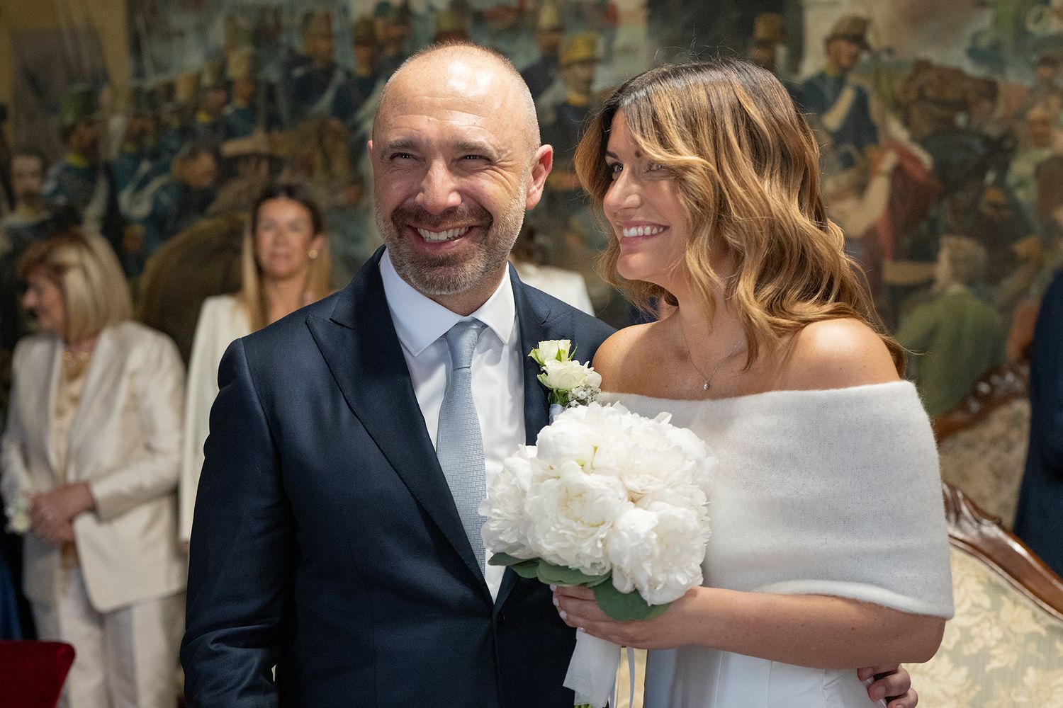 A joyful wedding couple sharing a moment together in front of a decorative mural wall.