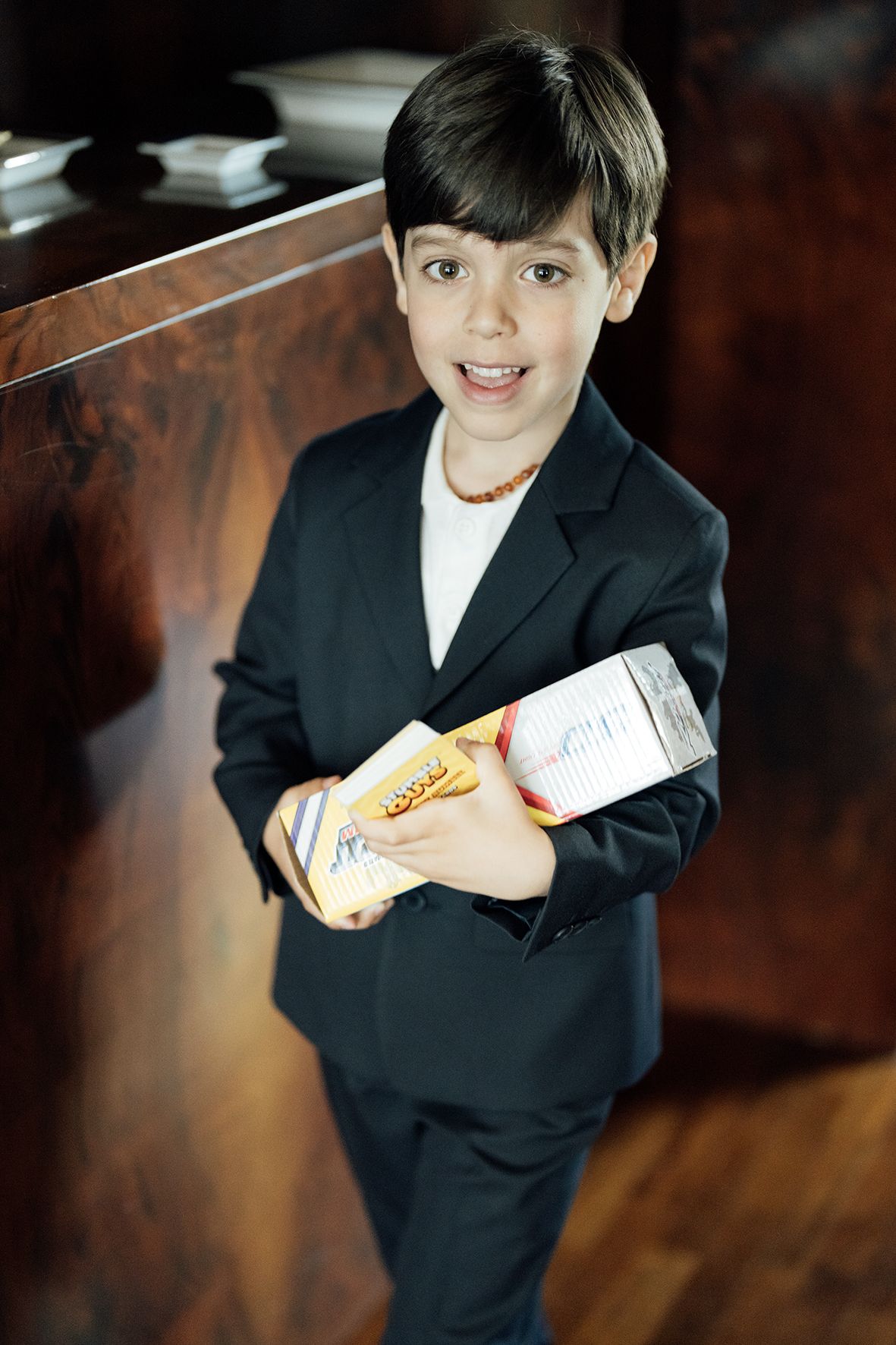 Young ring bearer in a black suit holding items during wedding ceremony.