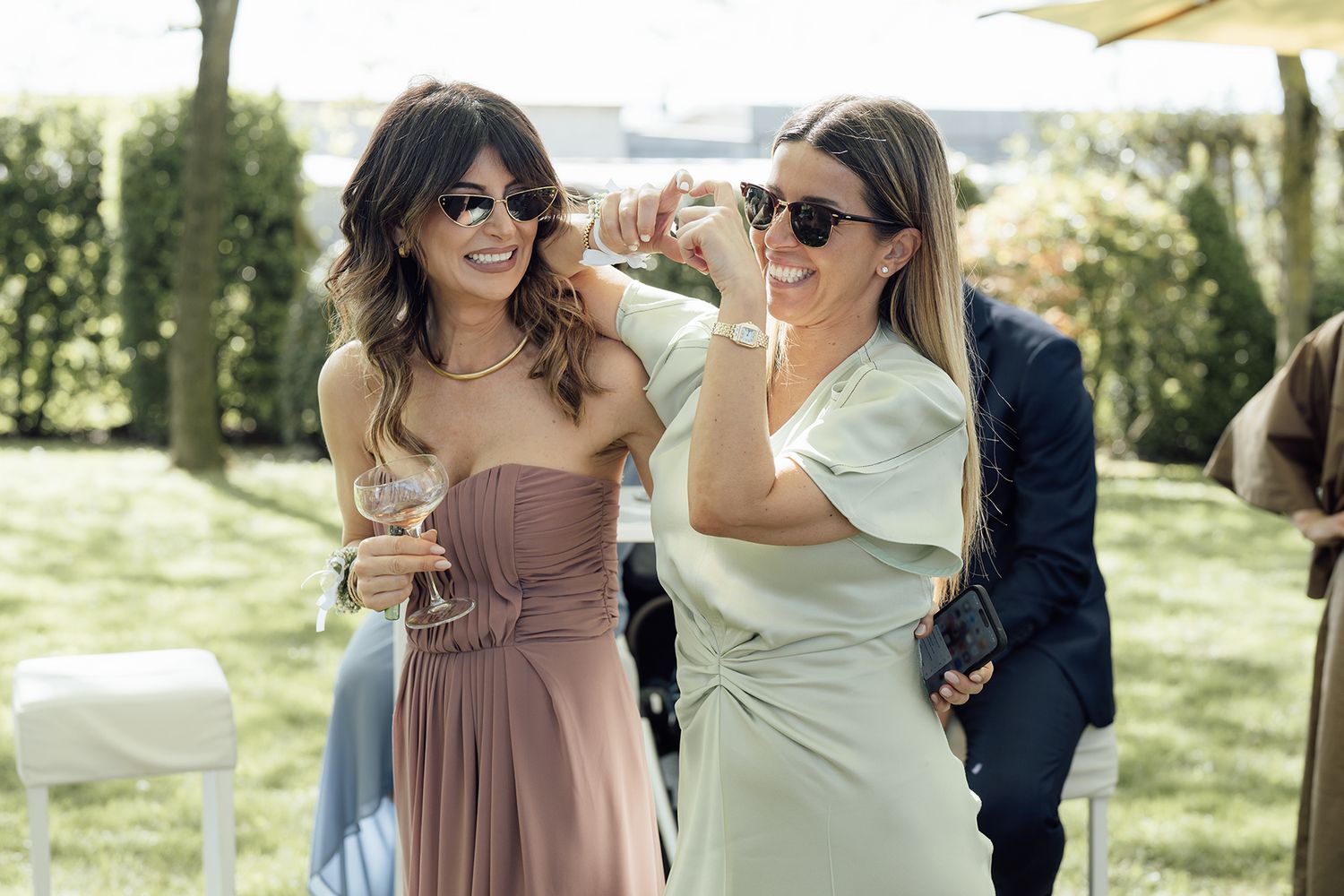 Group enjoying a sunny outdoor wedding celebration in formal attire.
