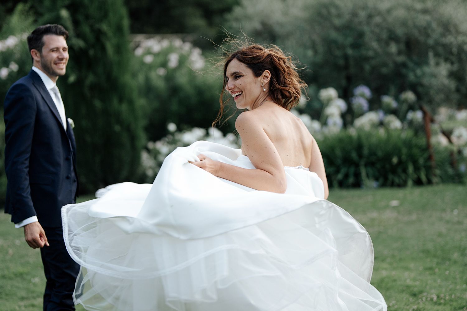 Elegant bride in flowing white dress twirling in a garden setting.