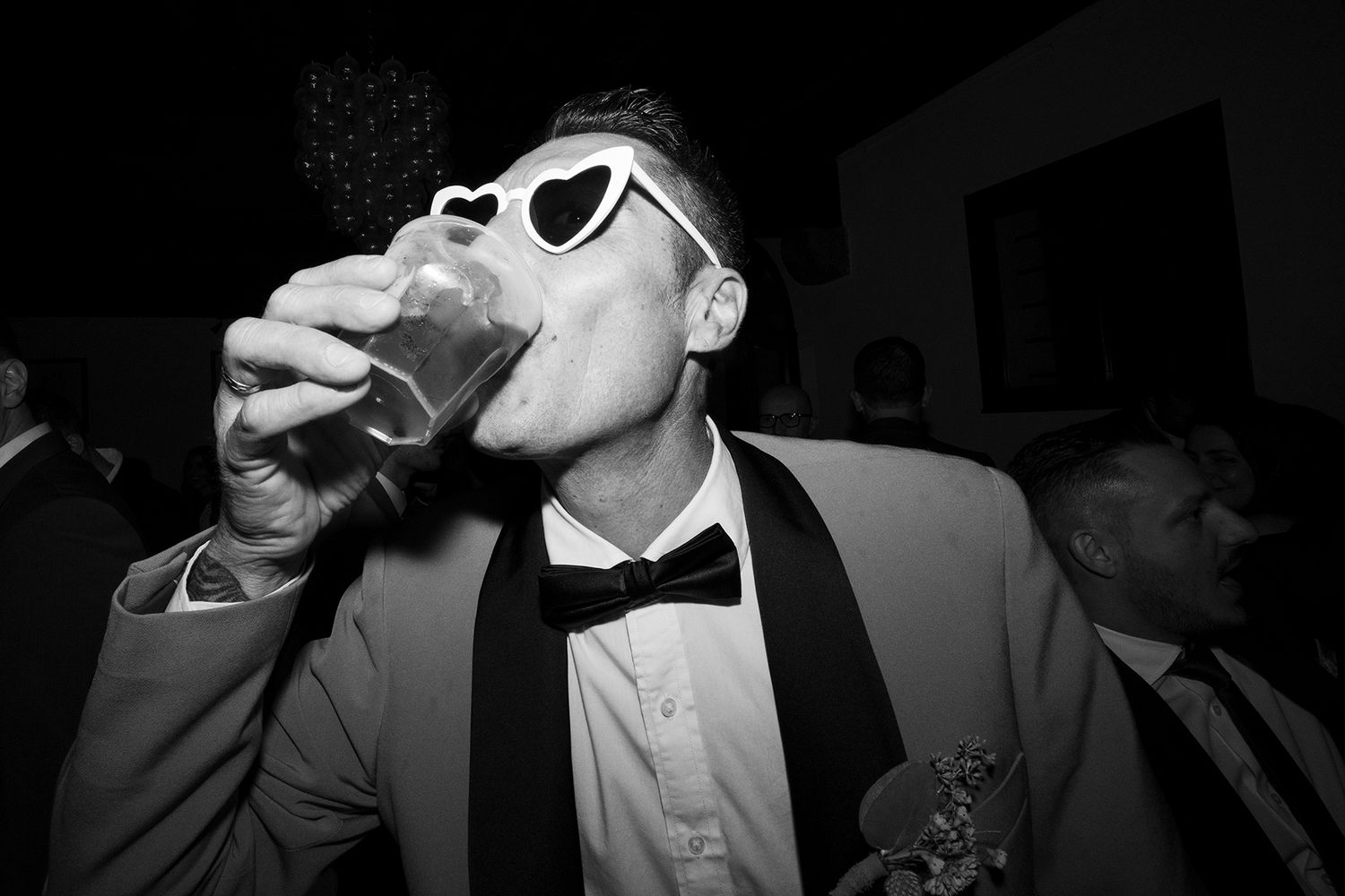 Party guests taking shots and celebrating at a formal event in black and white photography.
