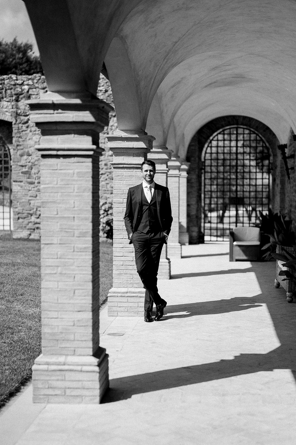 Black and white sequence of a person walking through a colonnade with arched shadows.