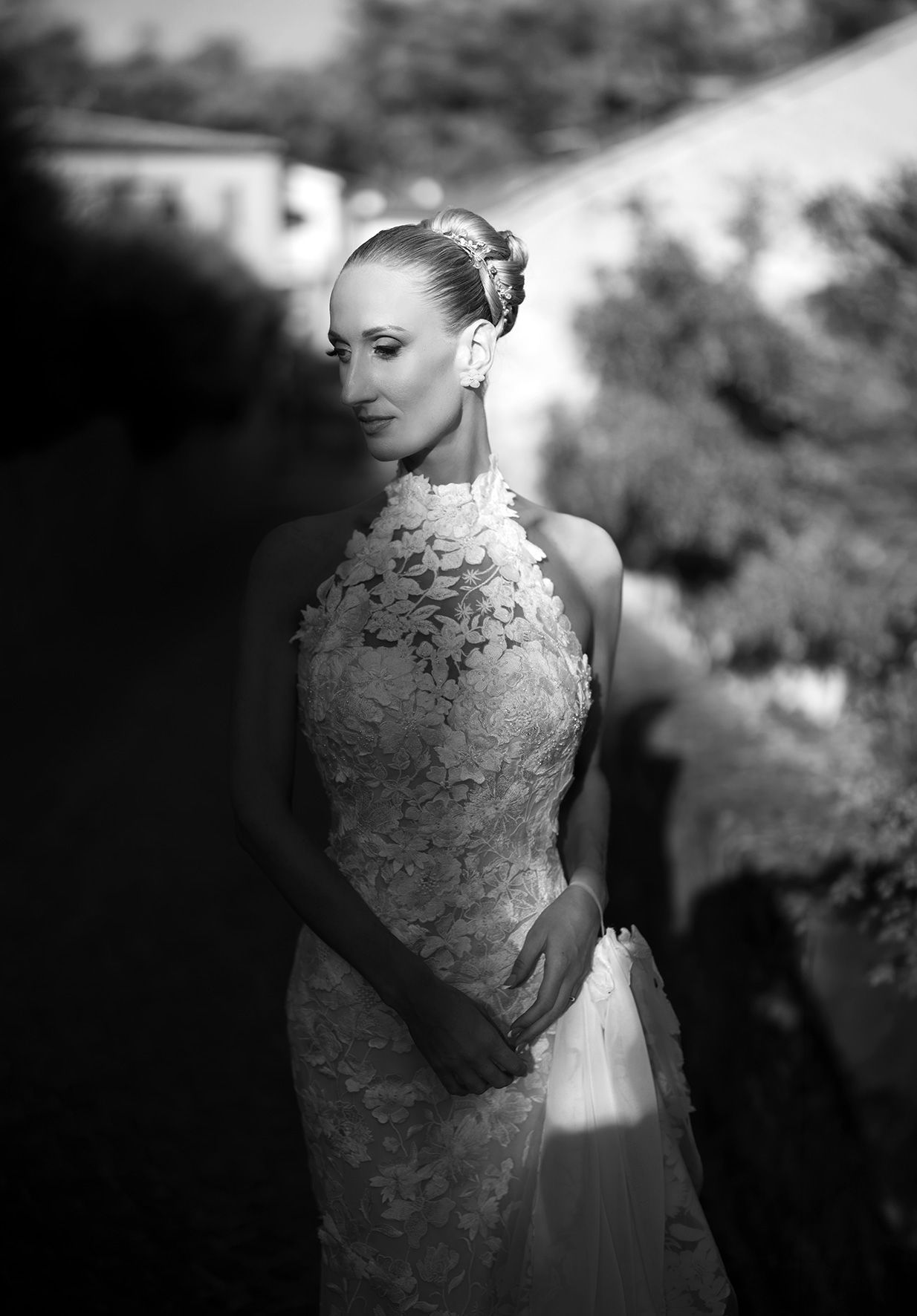 Elegant bride in lace halter wedding gown poses outdoors in black and white portrait photo.