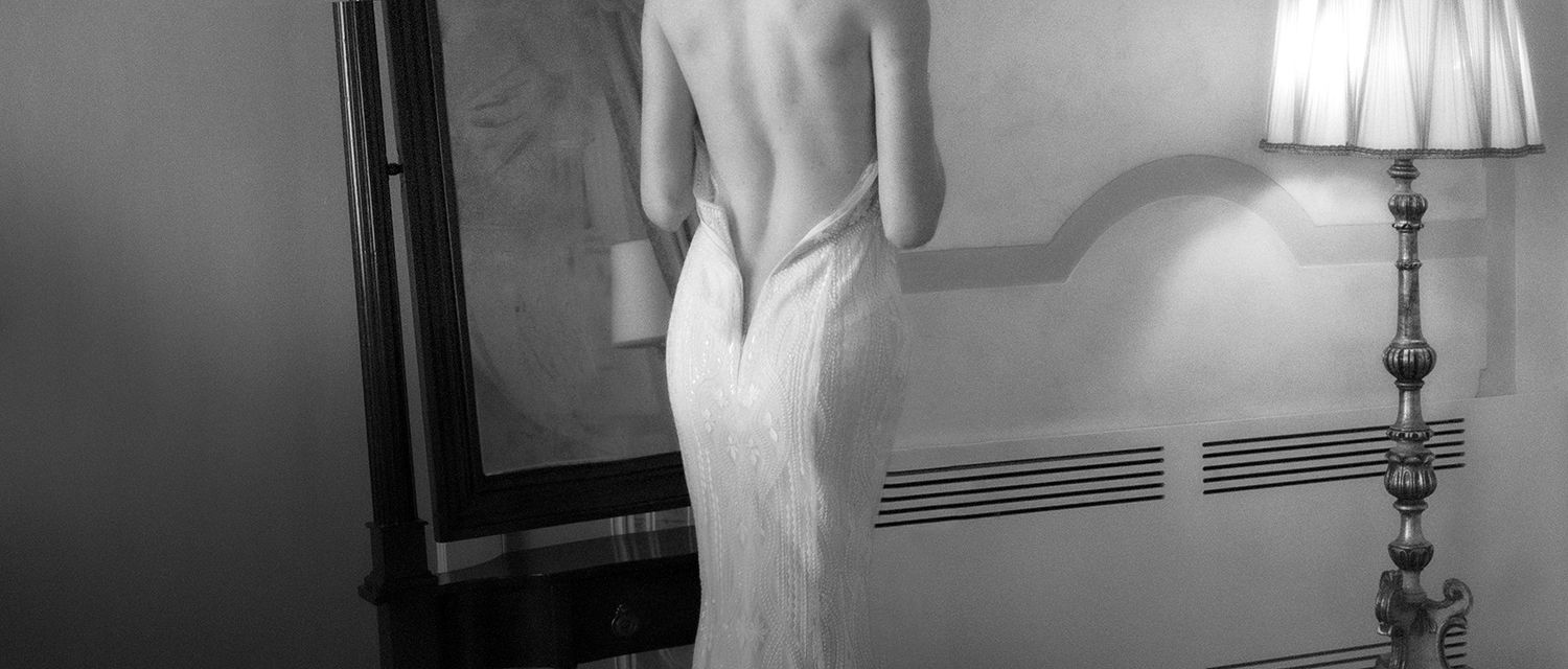 Elegant woman in a backless white lace gown poses gracefully in a black and white photograph.