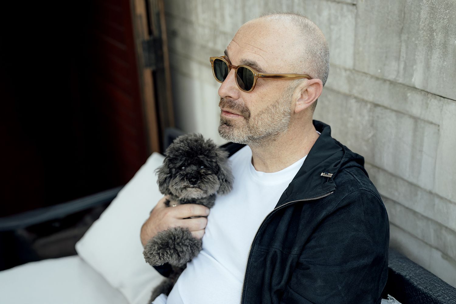 Person in sunglasses holding small grey dog while sitting outdoors.