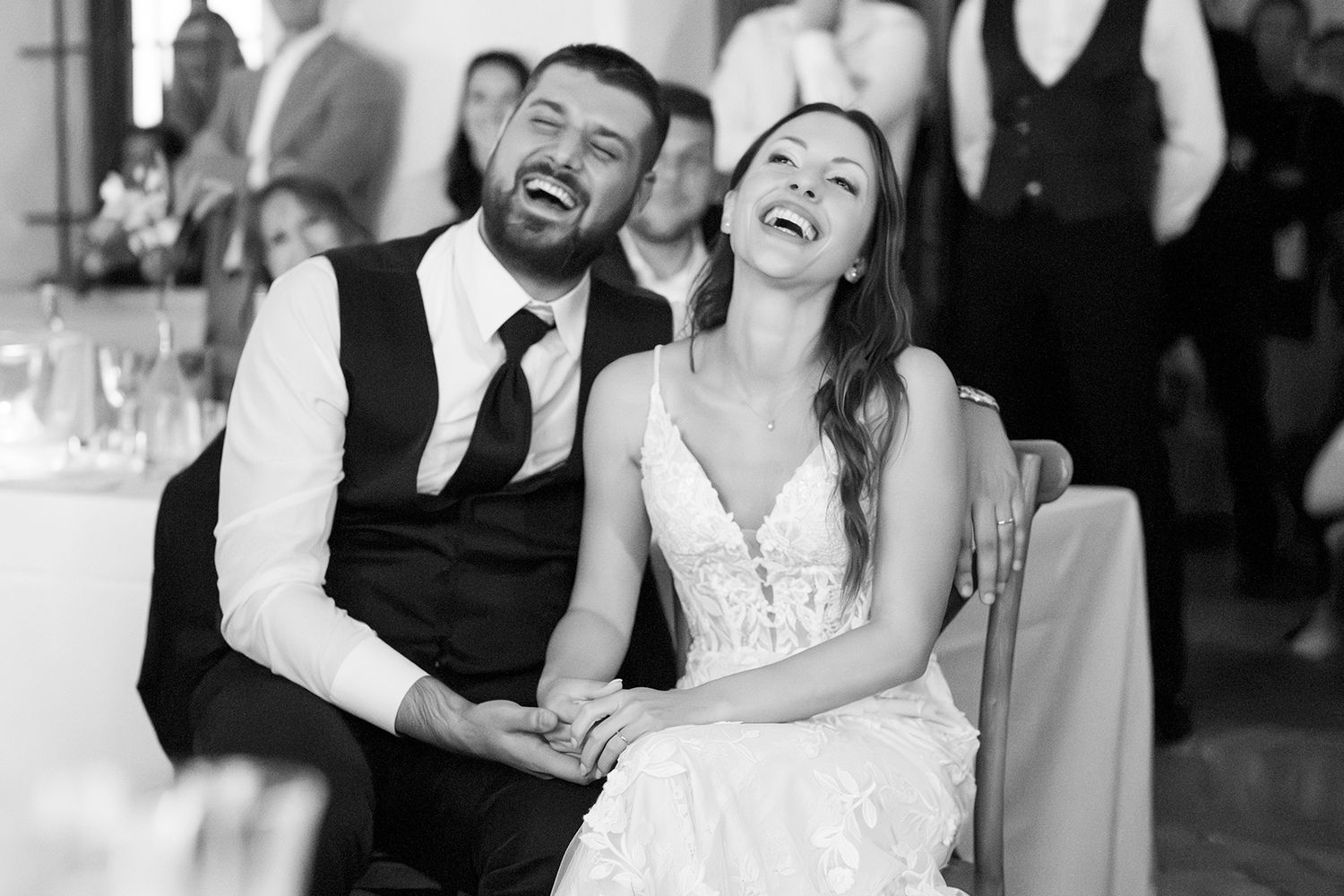 Candid black and white photo of joyful laughter during wedding reception celebrations.