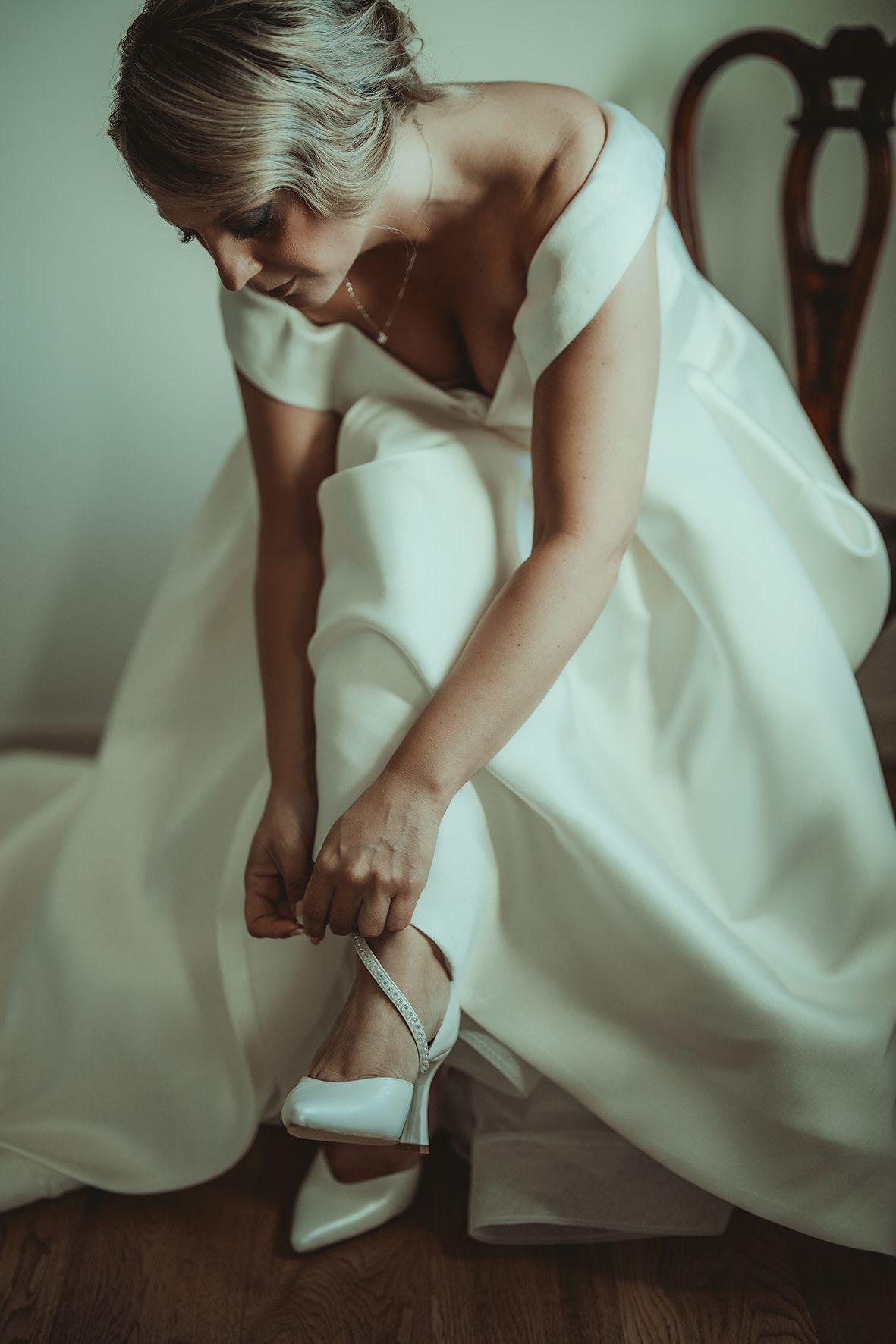 Close-up of bride adjusting her white heel while wearing flowing wedding dress.