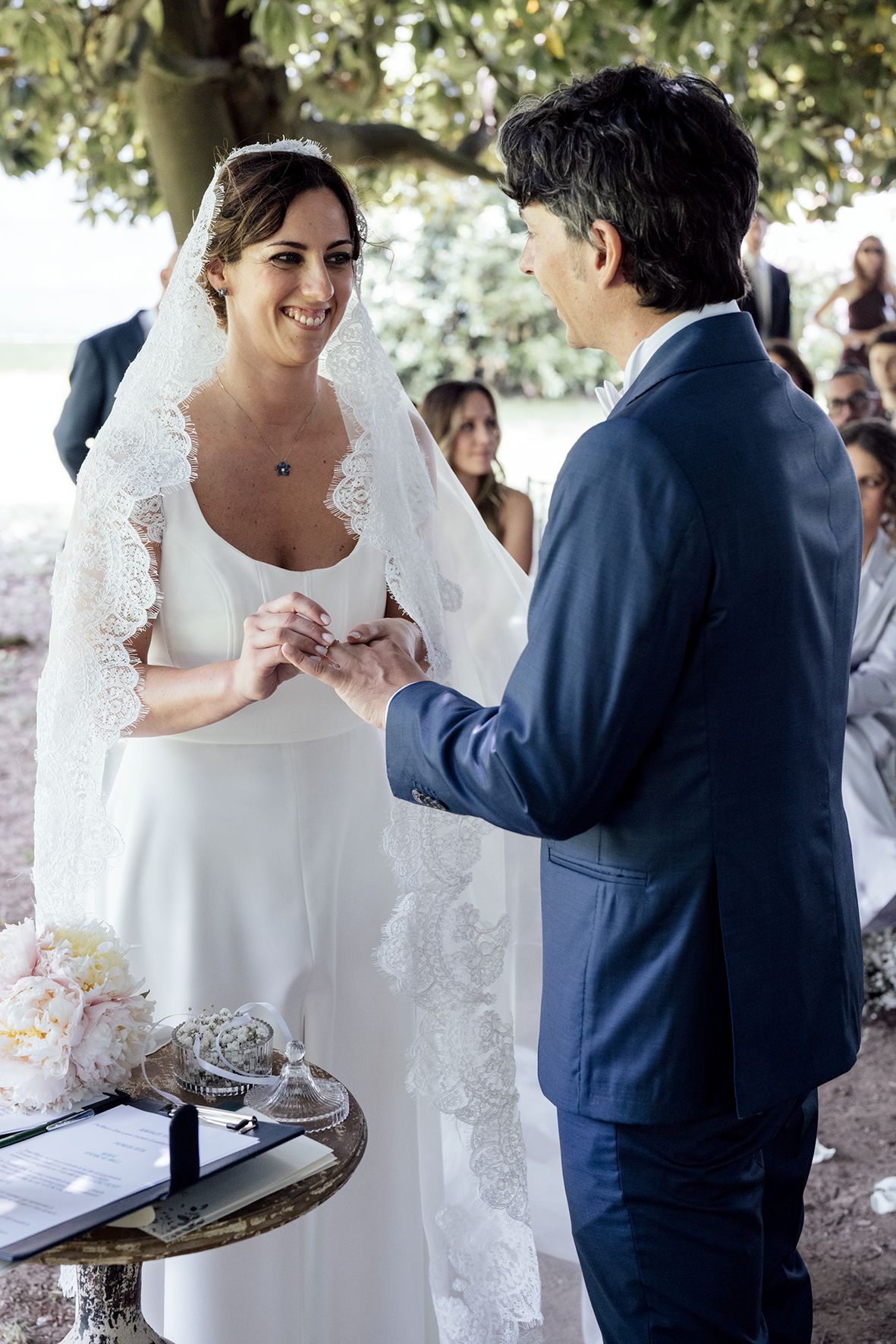 Couple reviewing wedding documents during outdoor ceremony under tree canopy.