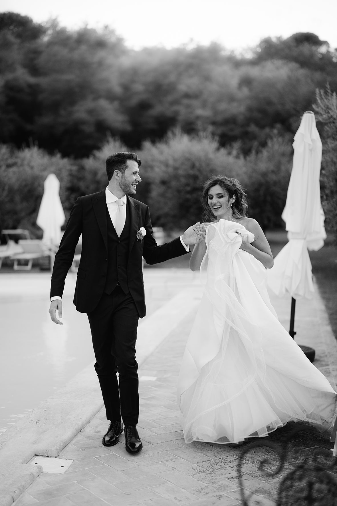 Black and white photo of newlyweds walking together with flowing wedding dress in motion.