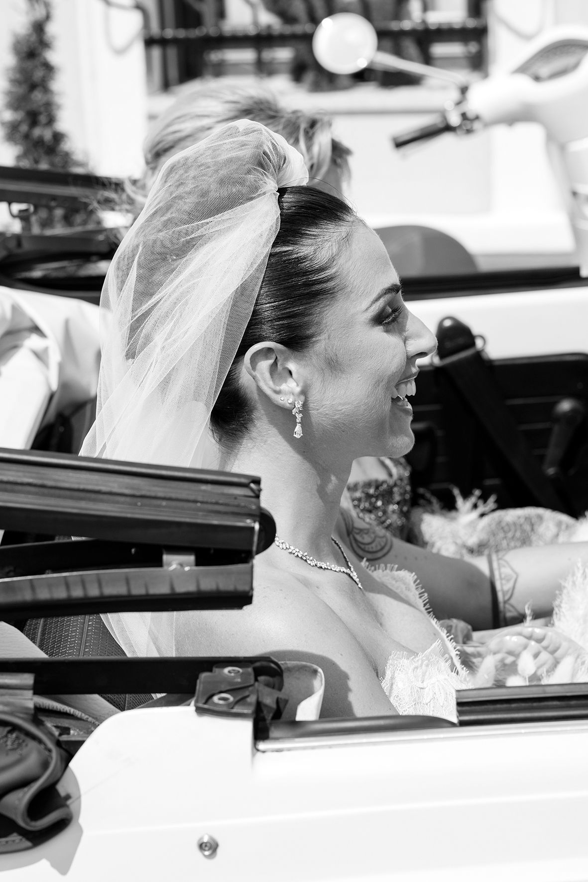 Bride in white veil smiling while seated in a car.