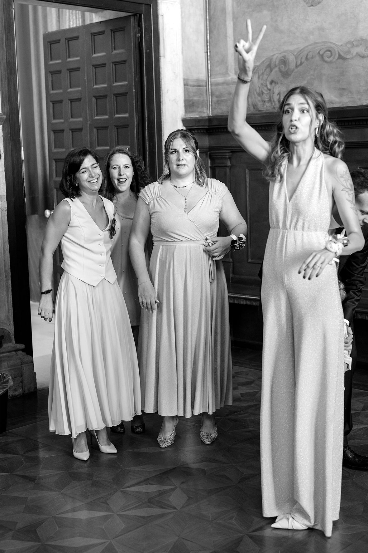 Black and white photo of bridesmaids in matching light dresses dancing indoors.