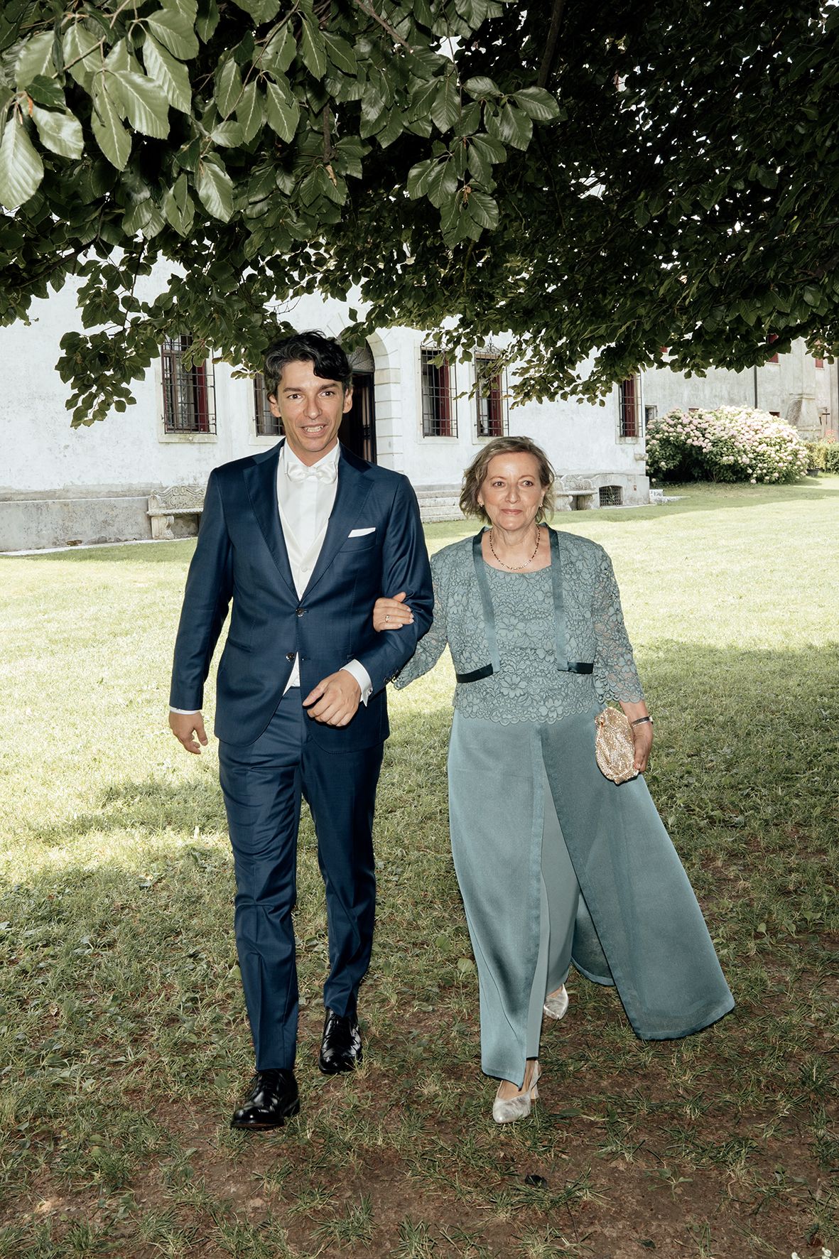 A couple walking together outdoors on a grassy area, with the person on the right wearing gray clothing.