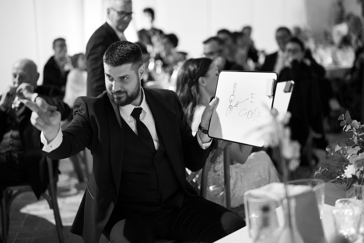 Black and white reception photo showing guests mingling at elegant indoor wedding venue.