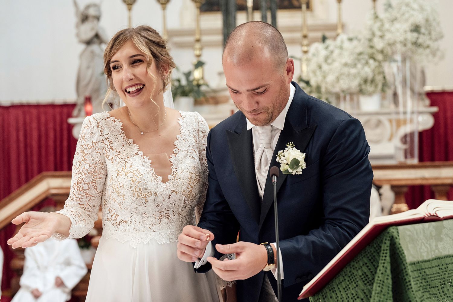 Bride in lace dress and groom in black suit share a candid moment at their wedding.