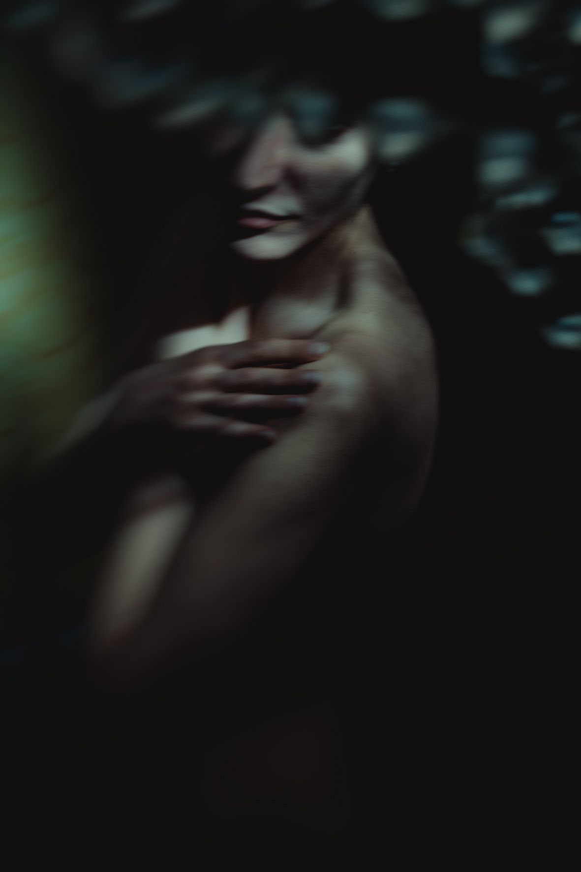 A mysterious dark artistic portrait of a person with flowing hair, arms crossed over chest in dramatic moody lighting.