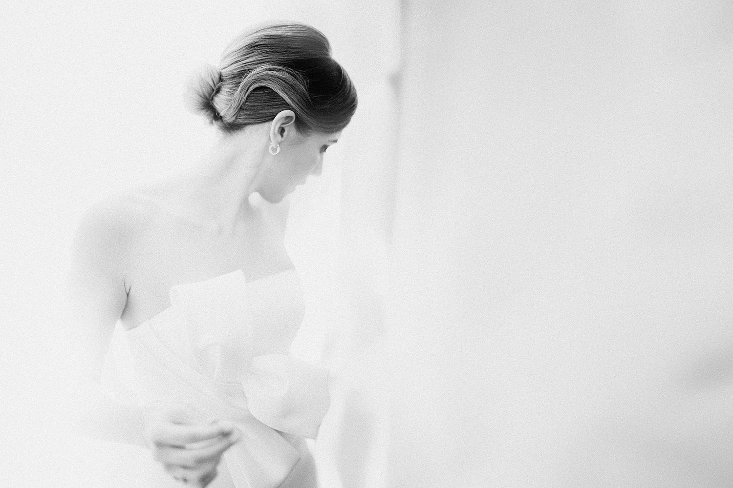 Elegant bride in strapless white gown with updo hairstyle, captured in soft black and white photography.