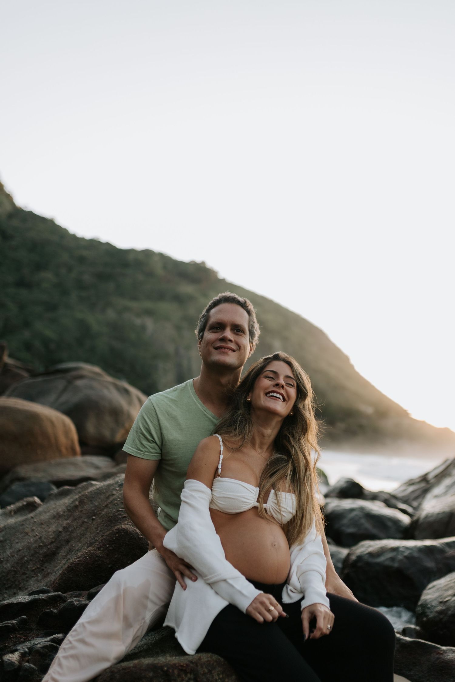 Happy couple sharing joyful moment on rocky coastal beach at sunset.