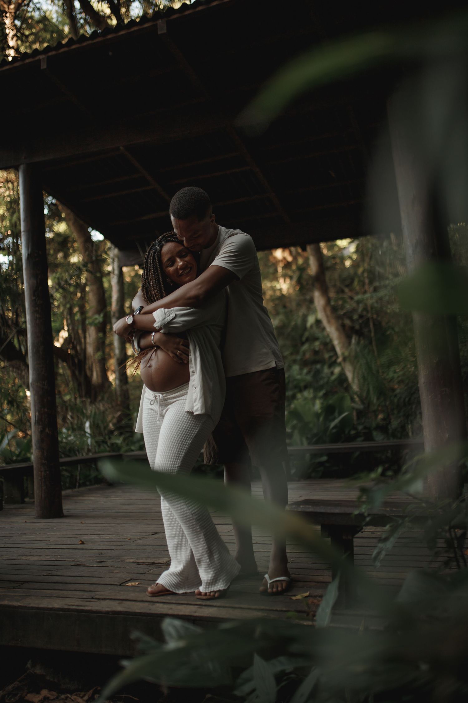 Intimate maternity moment captured on wooden deck surrounded by forest greenery.