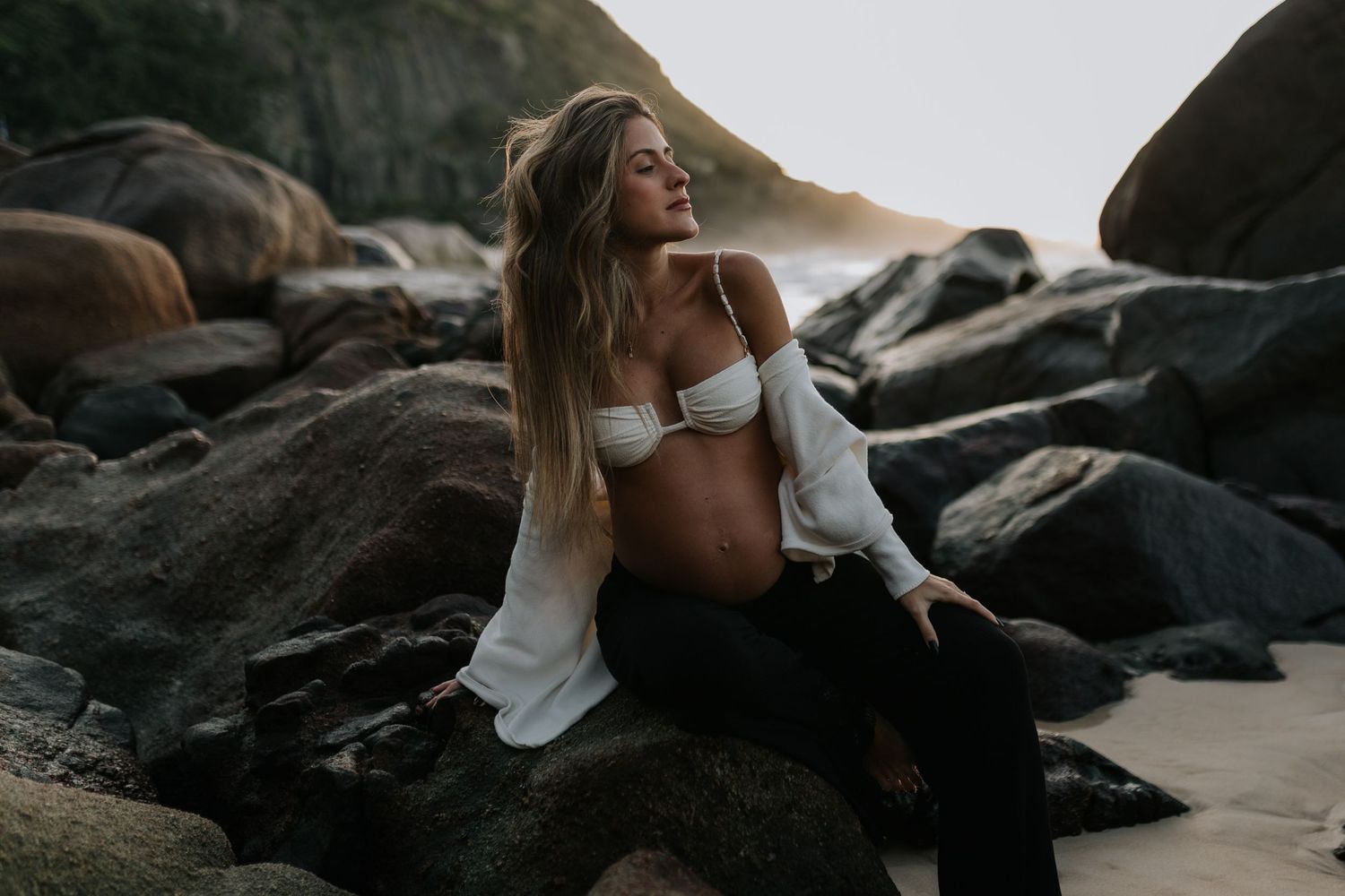 Person lounging on dark coastal rocks with dramatic ocean backdrop.
