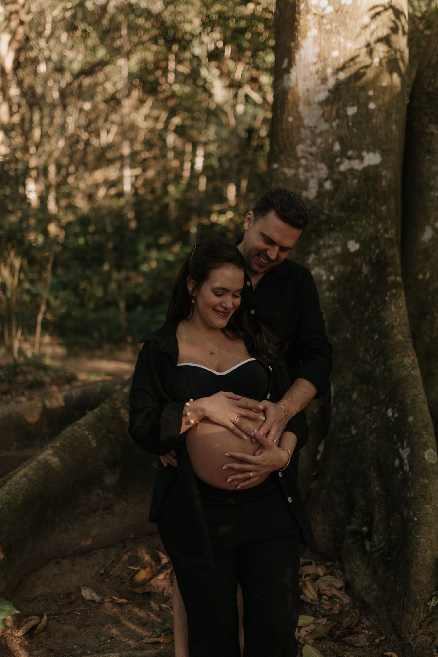 A couple shares tender moments in a wooded forest setting at dusk.