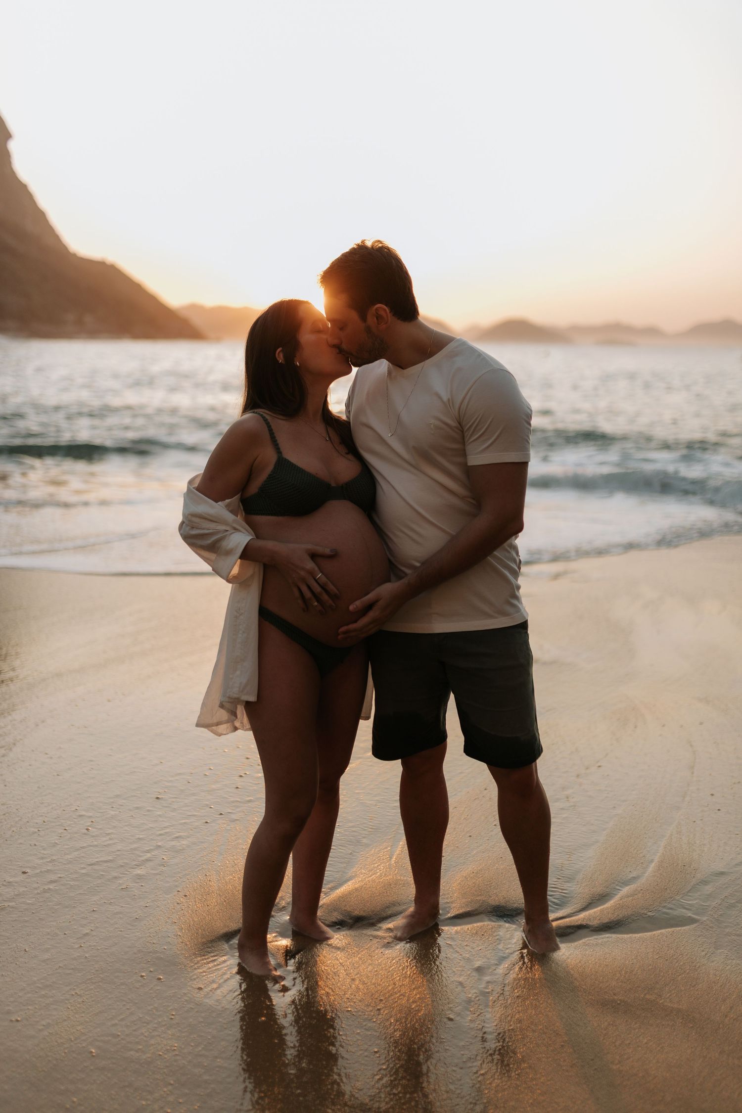 Expecting couple sharing intimate moment on beach at sunset.