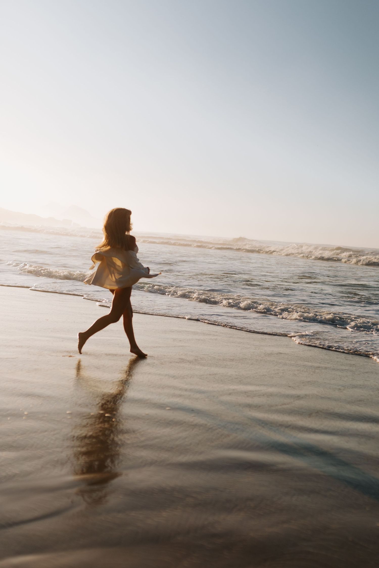 Silhouette of someone running along wet beach sand at sunset.