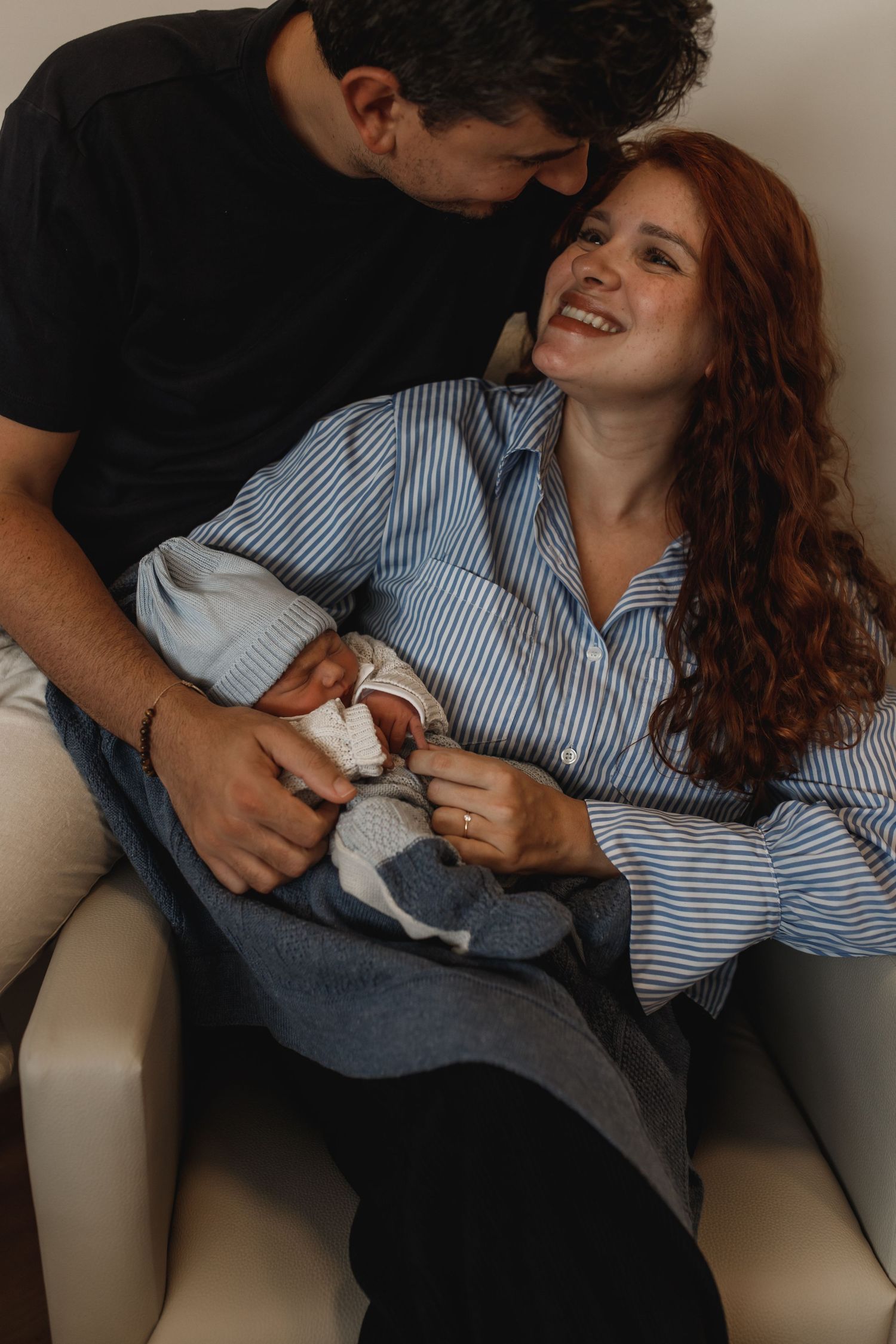 Candid moment of parents lounging on couch with their newborn baby.