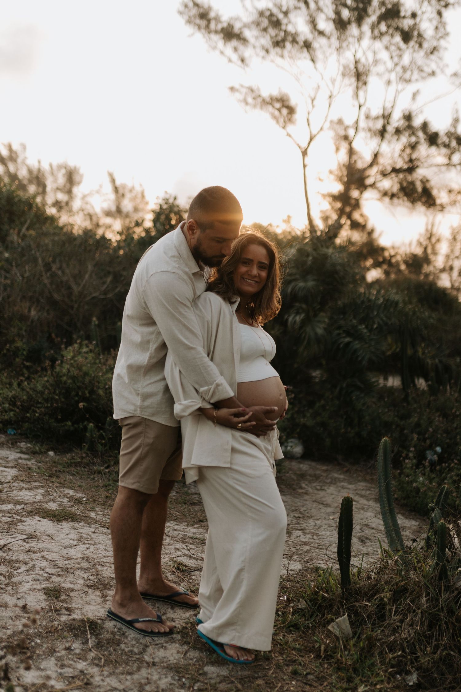 Couple embracing on sandy path during golden hour with natural foliage in background.