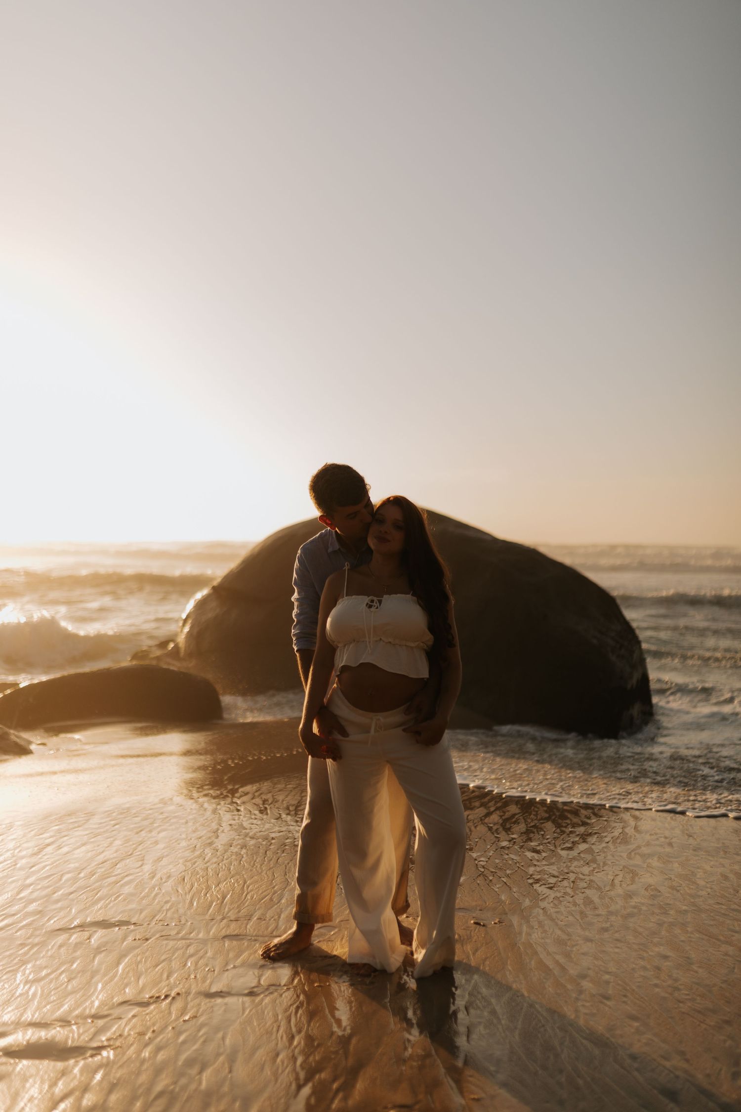 Person in white clothing exploring tidal pools and rocks along ocean shoreline at dusk.