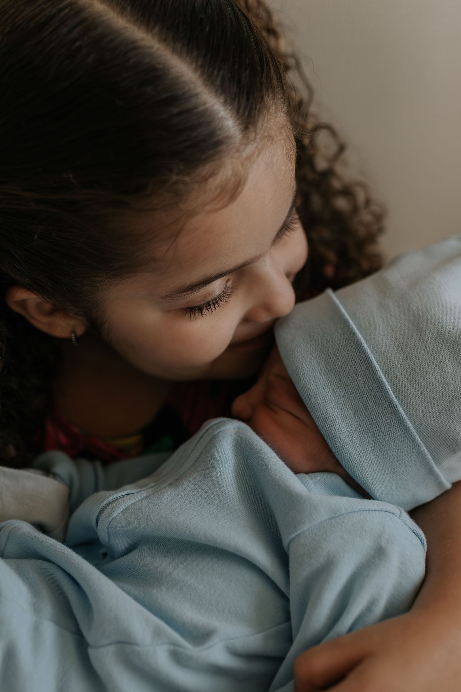 A close-up view of someone gently cradling a baby wrapped in soft blue fabric.