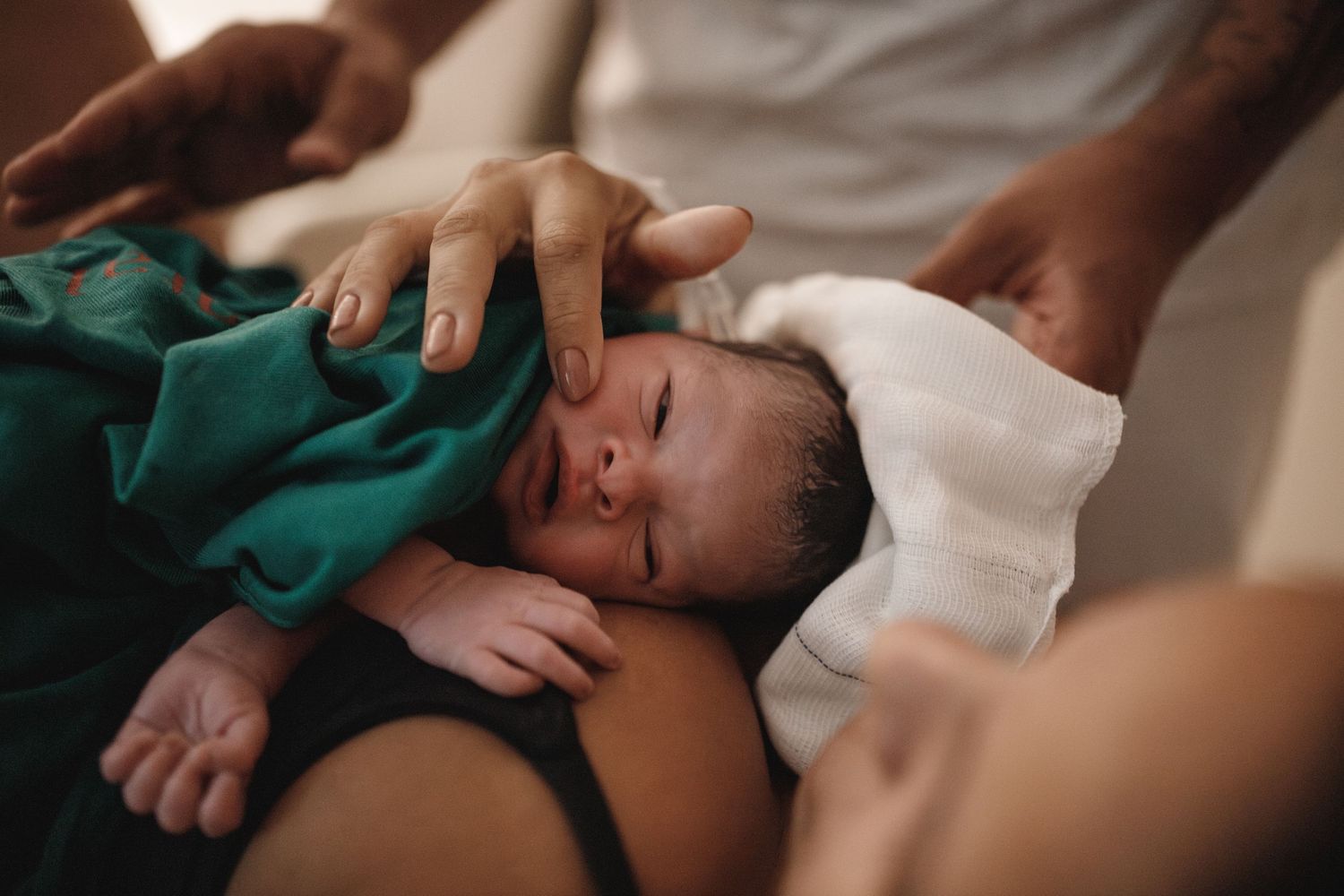 A newborn baby swaddled in a green and white blanket during a medical examination.
