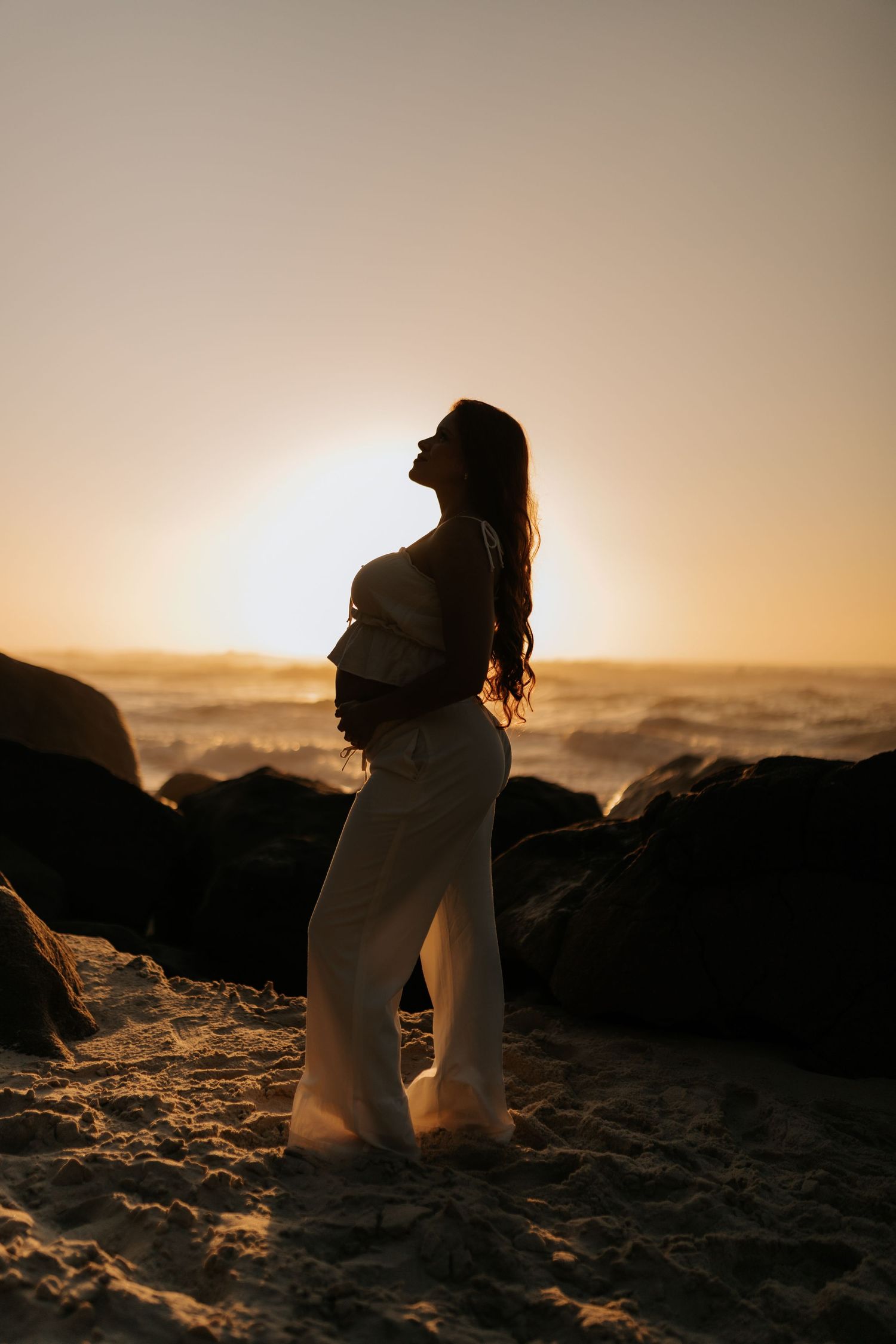 Dramatic silhouette of person in flowing dress on sandy beach during sunset.