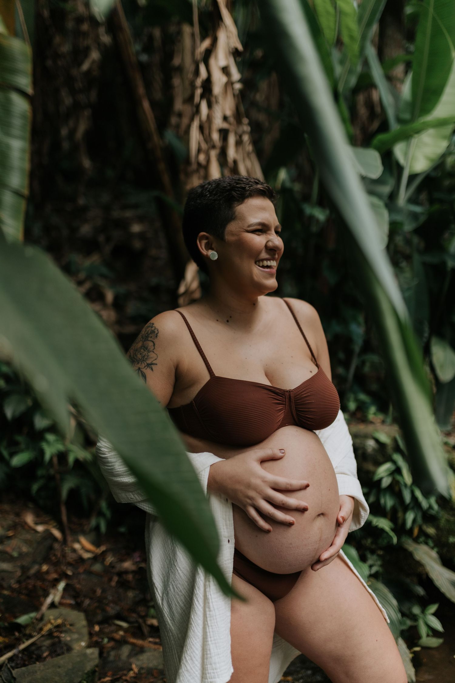 Maternity photoshoot in lush tropical garden setting with natural lighting.